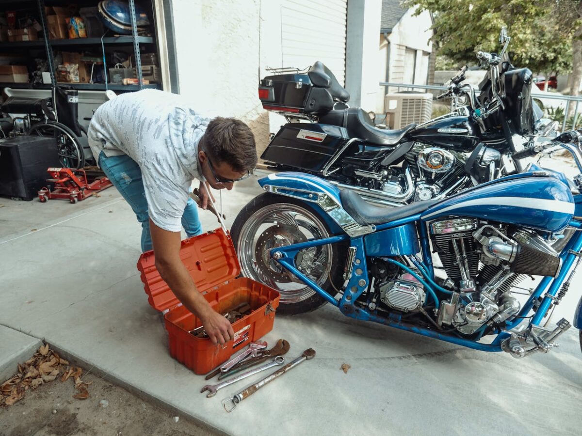 Man working on motorcycle repair with tools in a garage setting.